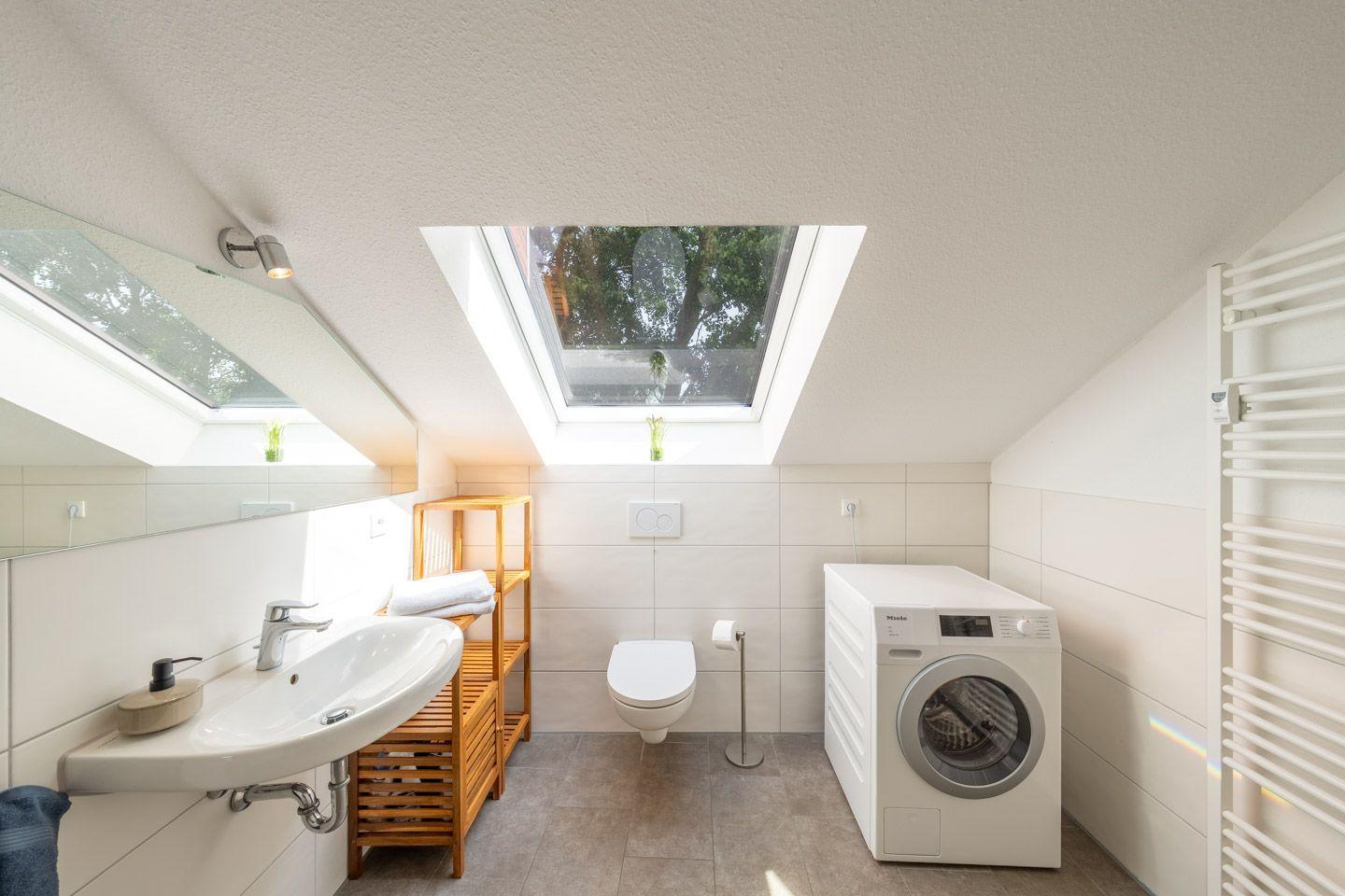 Badezimmer mit Waschmaschine, Toilette und Dachfenster. Holzregal und Spiegel.