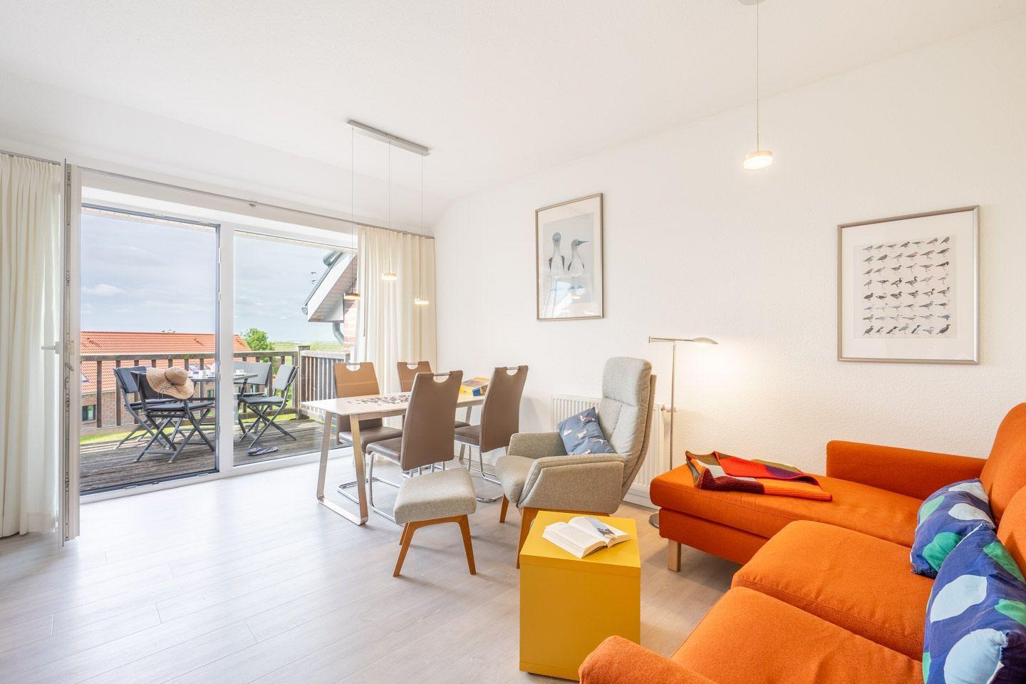 Wohn- und Essbereich mit Balkon, orange Sofa und Esstisch mit Stühlen.