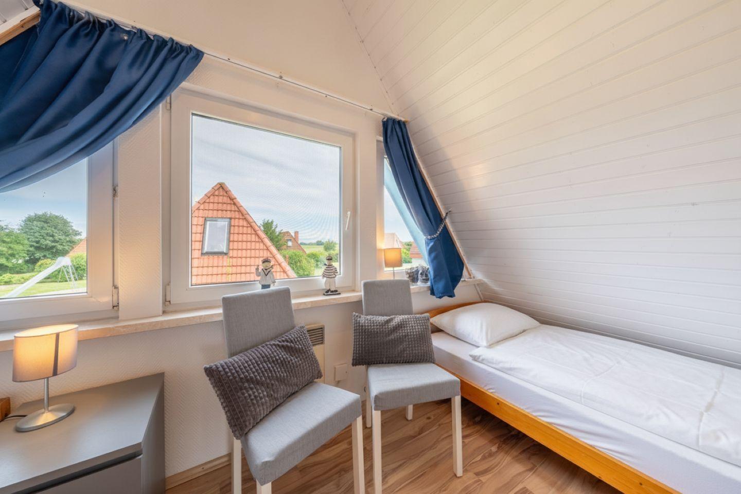 Ein Schlafzimmer mit einem Bett, zwei Stühlen und einem Fenster mit Blick auf ein Haus.