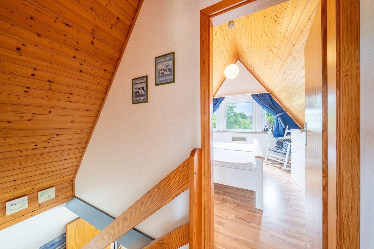 Durchgang in Schlafzimmer mit Holzdecke, Bett und Fenster mit blauen Vorhängen.