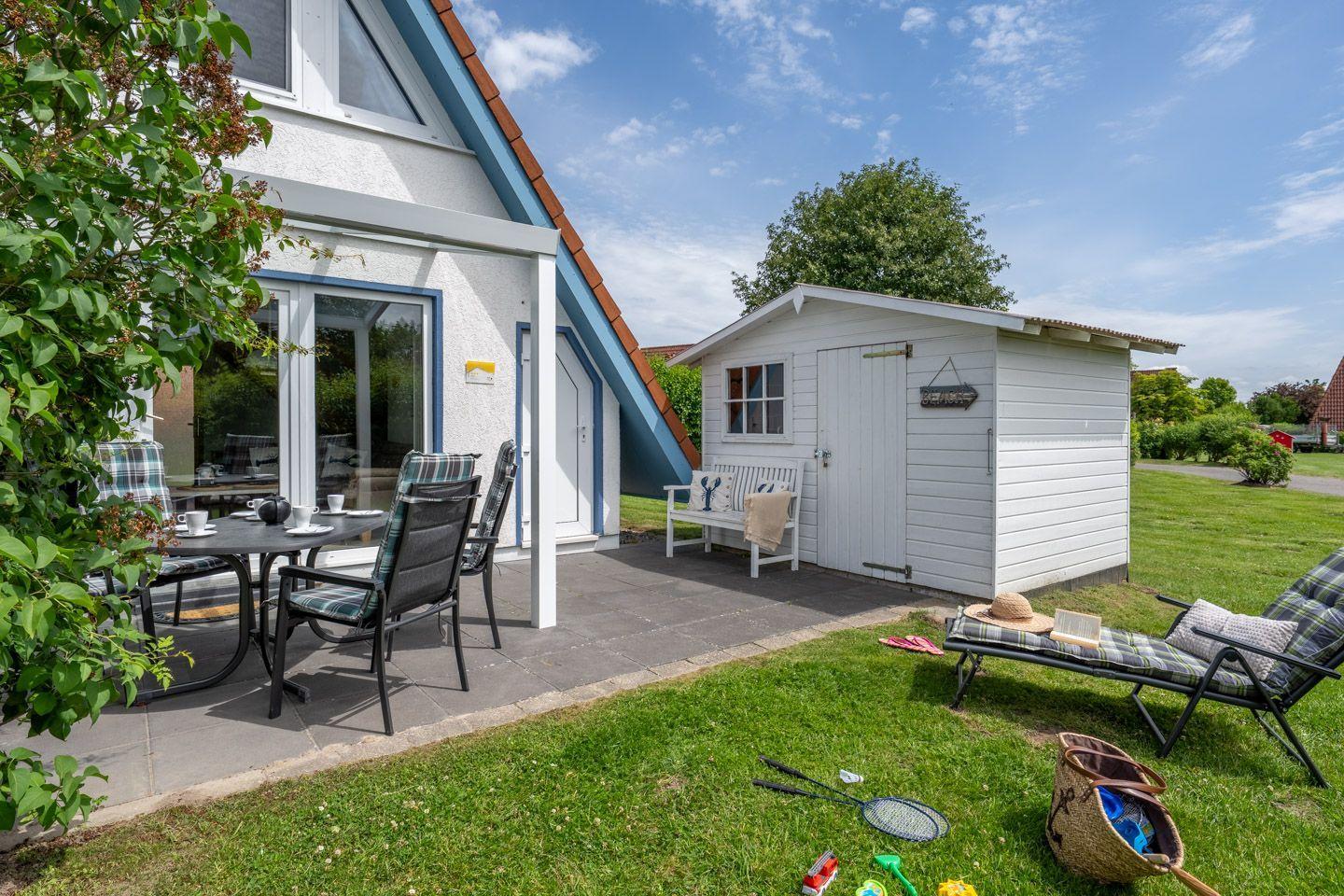 Terrasse mit Tisch und Stühlen, Gartenliege und kleinem Holzschuppen.