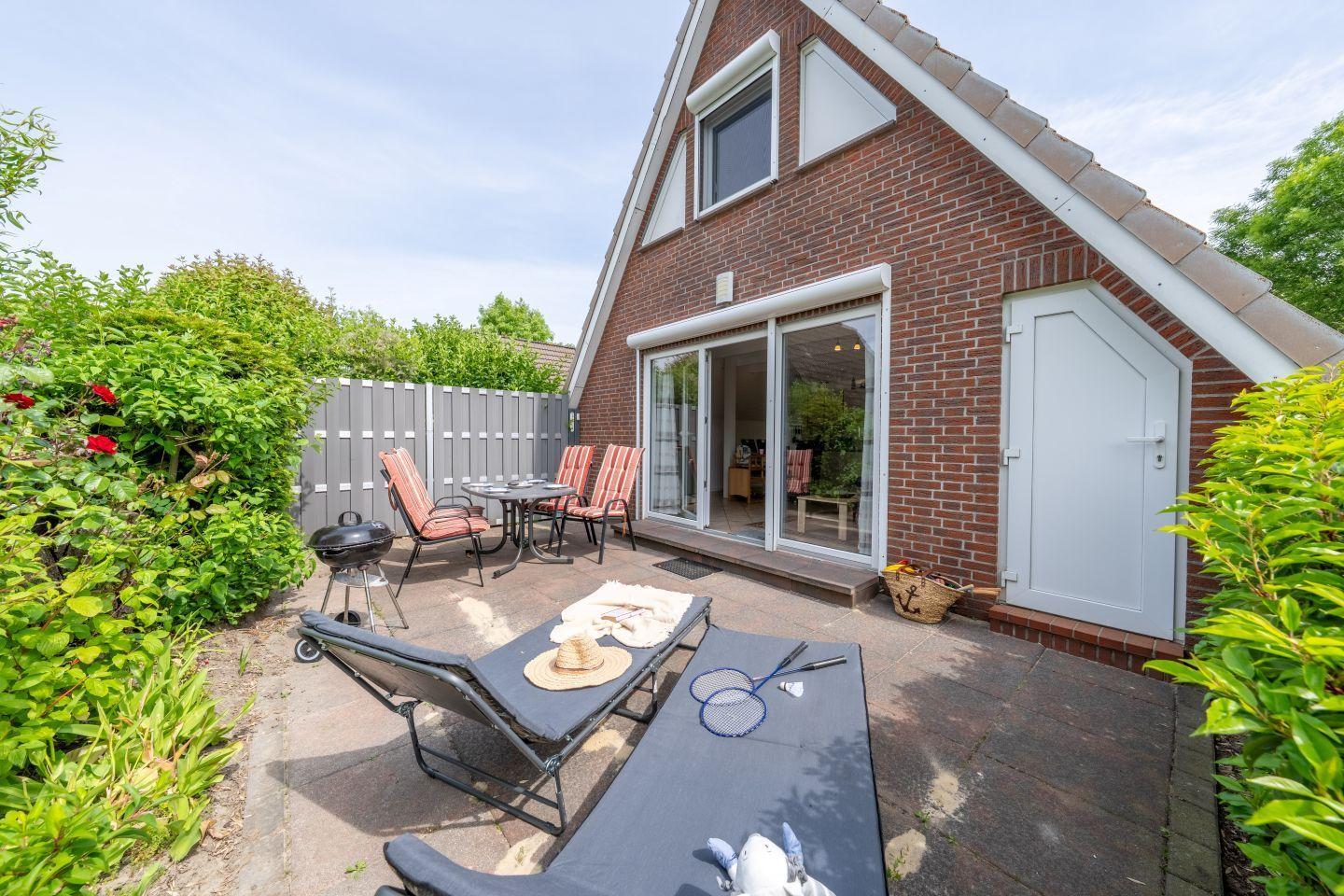 Terrace with loungers, grill, and table. Door leads into the house. Surrounded by greenery.