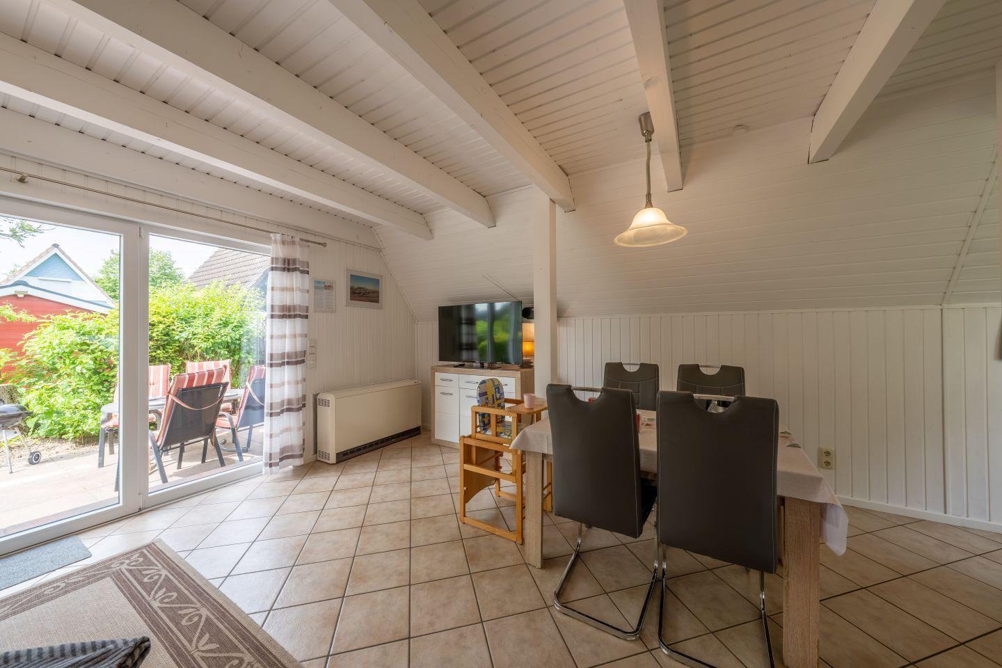 Dining area with table and chairs, TV, and door to the garden.