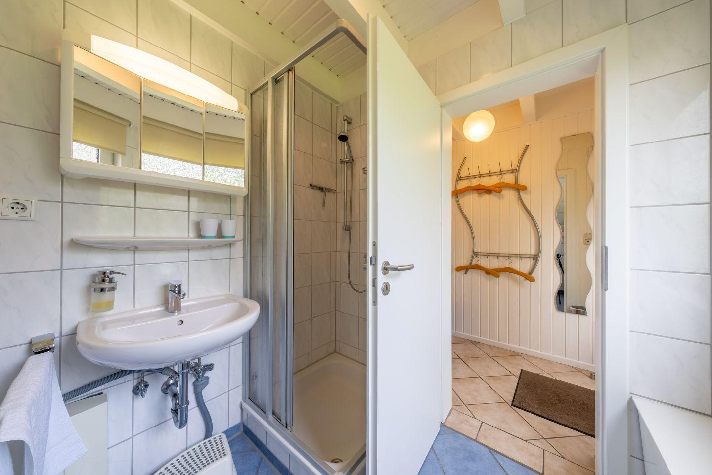 Bathroom with shower, sink, and mirror. Passage to a hallway with coat rack.