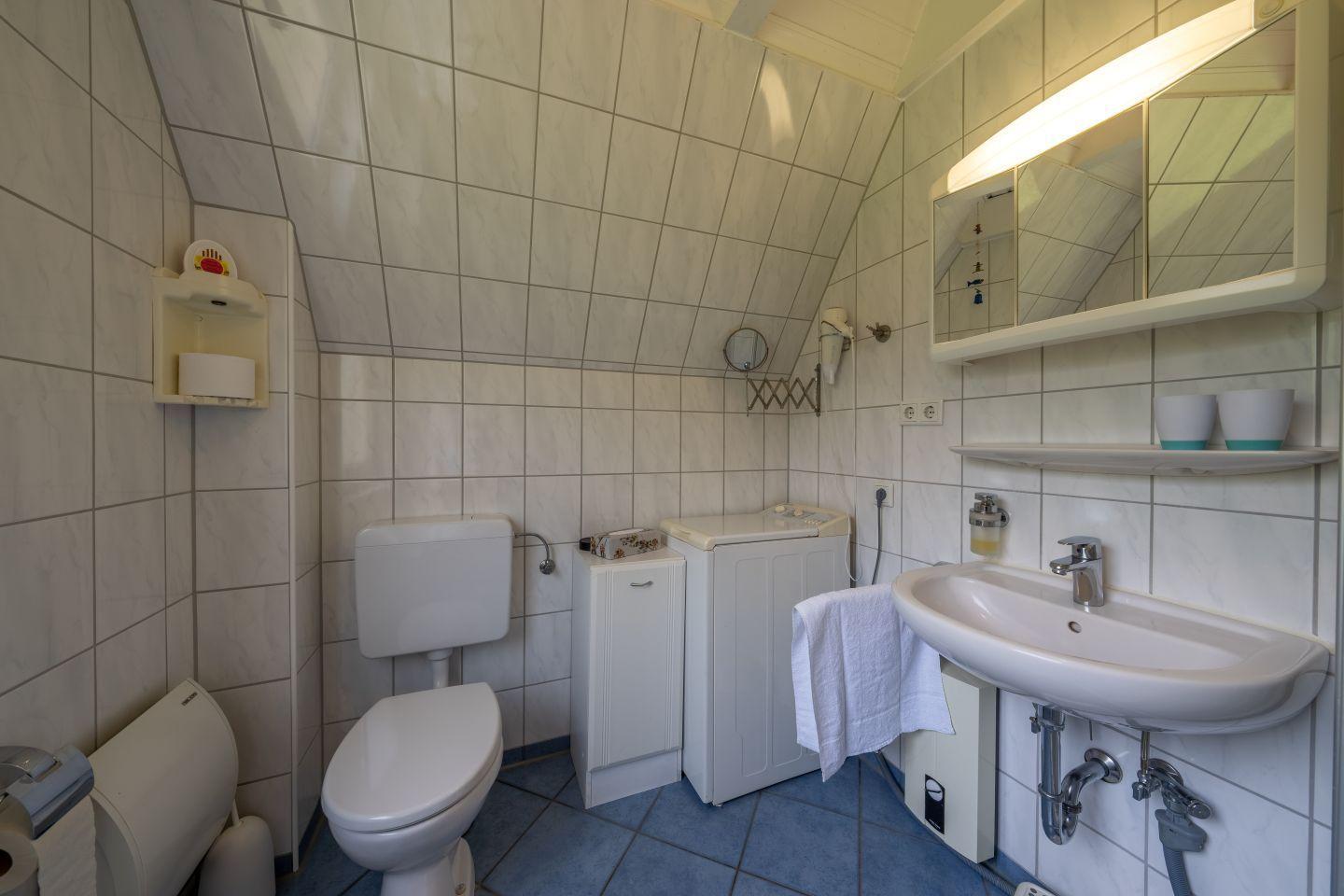 Bathroom with toilet, washing machine, and sink under mirror.