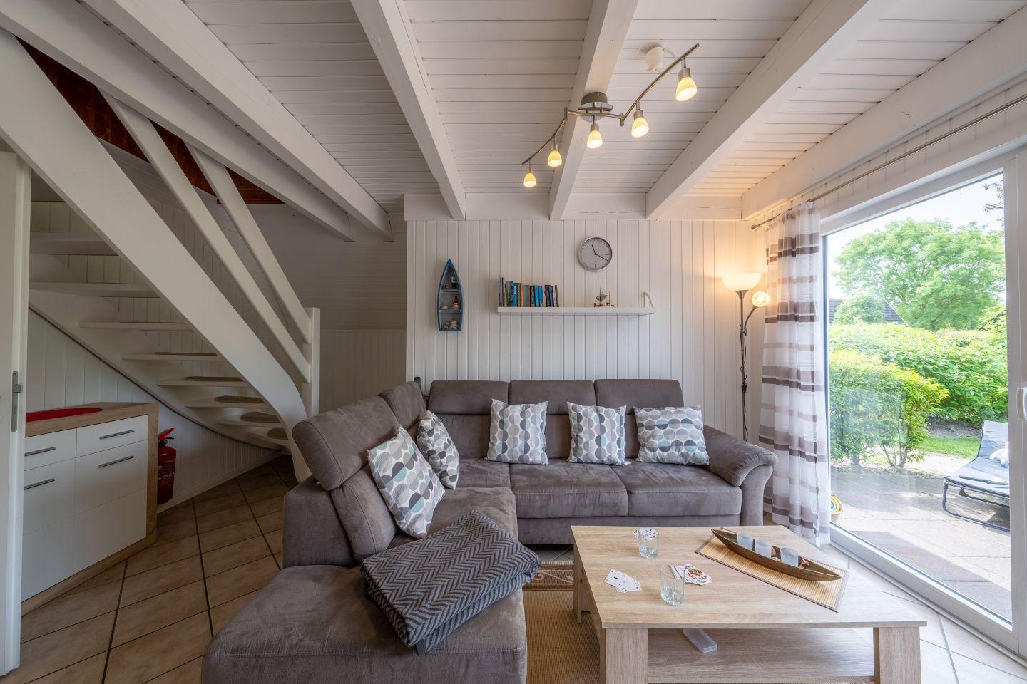 Living room with sofa, coffee table, and terrace door. Wooden ceiling and staircase visible.