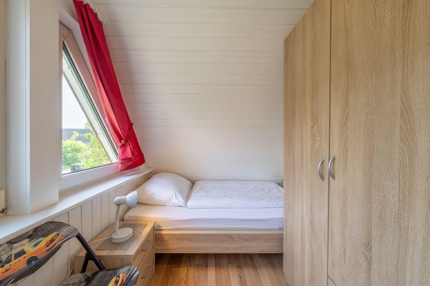 Bedroom with double bed, wardrobe, and window with red curtain.