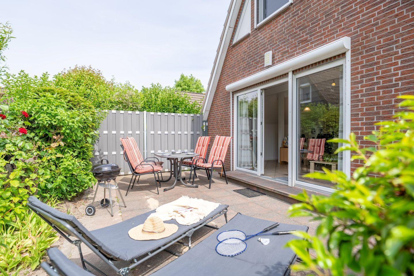 Terrace with lounge chairs, table, chairs, and grill. Sliding glass doors lead to the house.