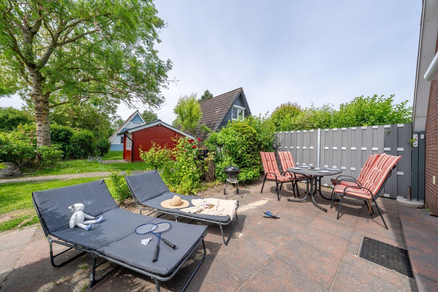 Terrace with loungers, table, chairs, and grill. Backyard with fence and trees.