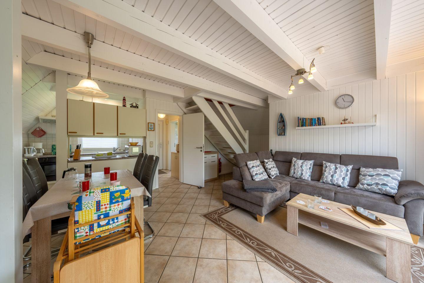 Living and dining area with sofa, table, and kitchen. Wooden ceiling and staircase visible.