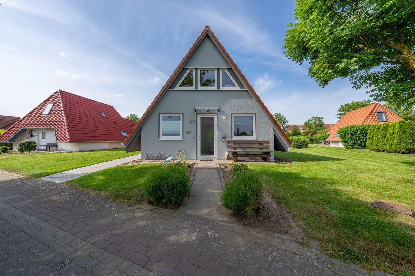 Ein graues Haus mit rotem Dach, Vorgarten und Holzbank vor der Tür.