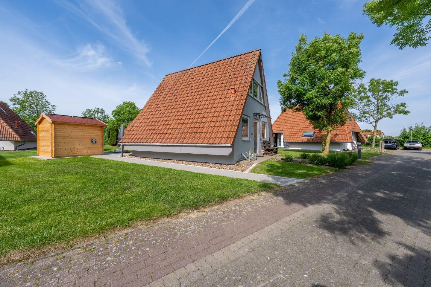 Moderne Ferienhaus mit rotem Dach und grünem Garten. Nebenhaus und Parkplatz sind sichtbar.
