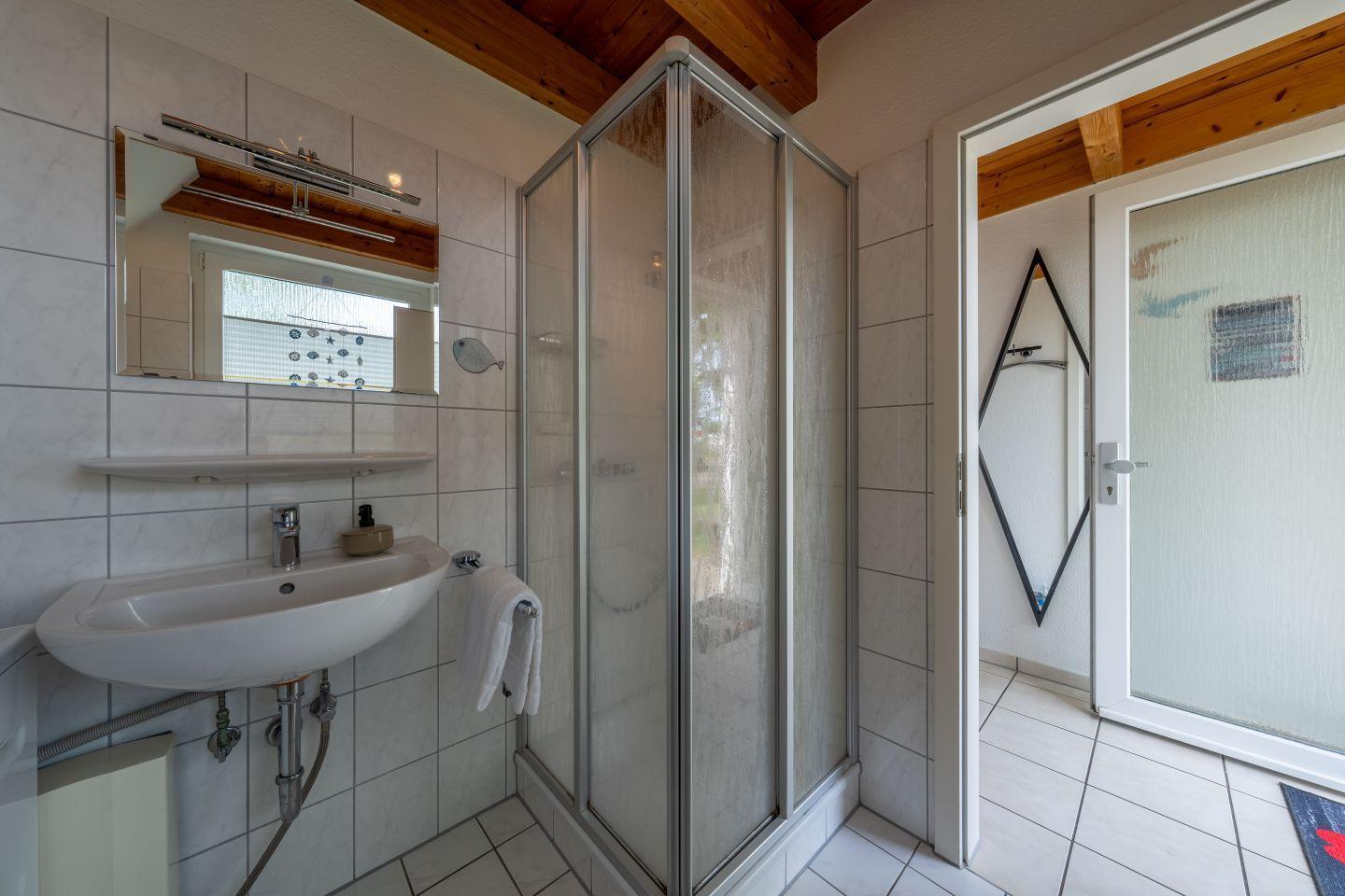 Badezimmer mit Dusche, Waschbecken und Spiegel. Holzdecken und Fliesen.
