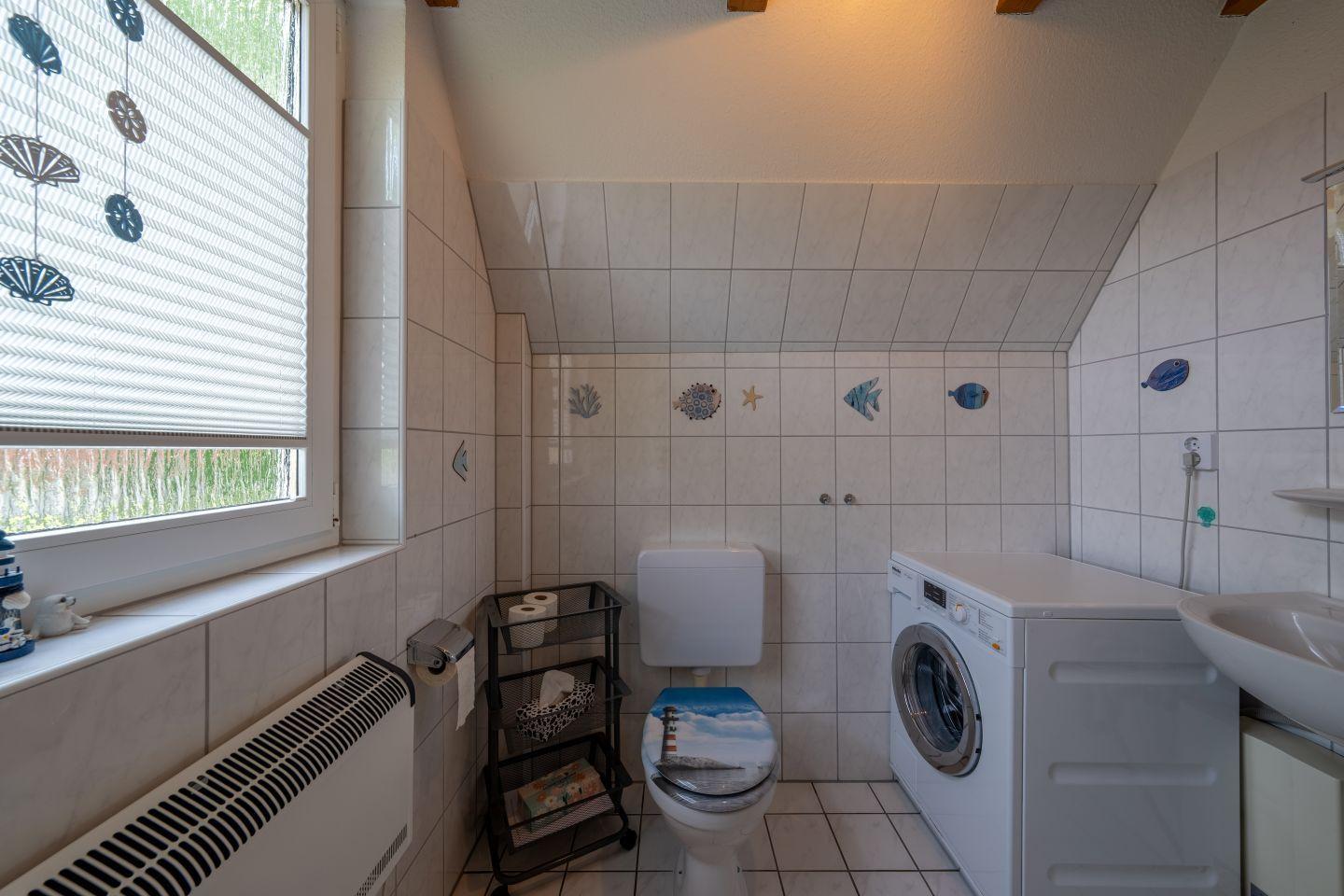 Badezimmer mit Toilette, Waschmaschine und Fenster mit Seetang-Dekoration.
