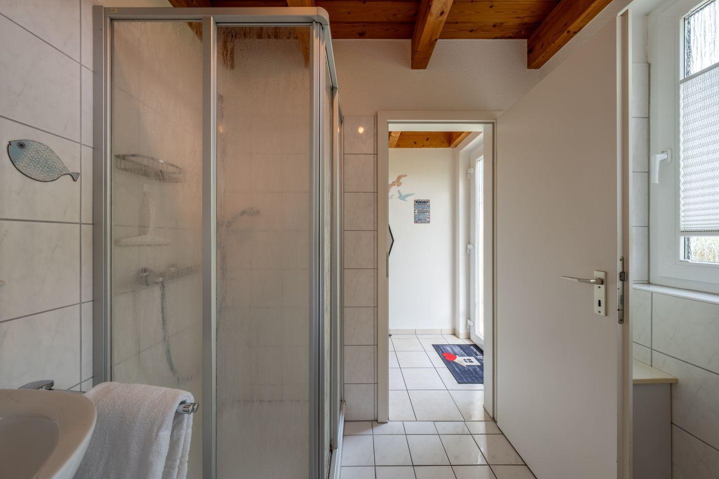 Badezimmer mit Dusche, Fenster und Blick in den Flur.