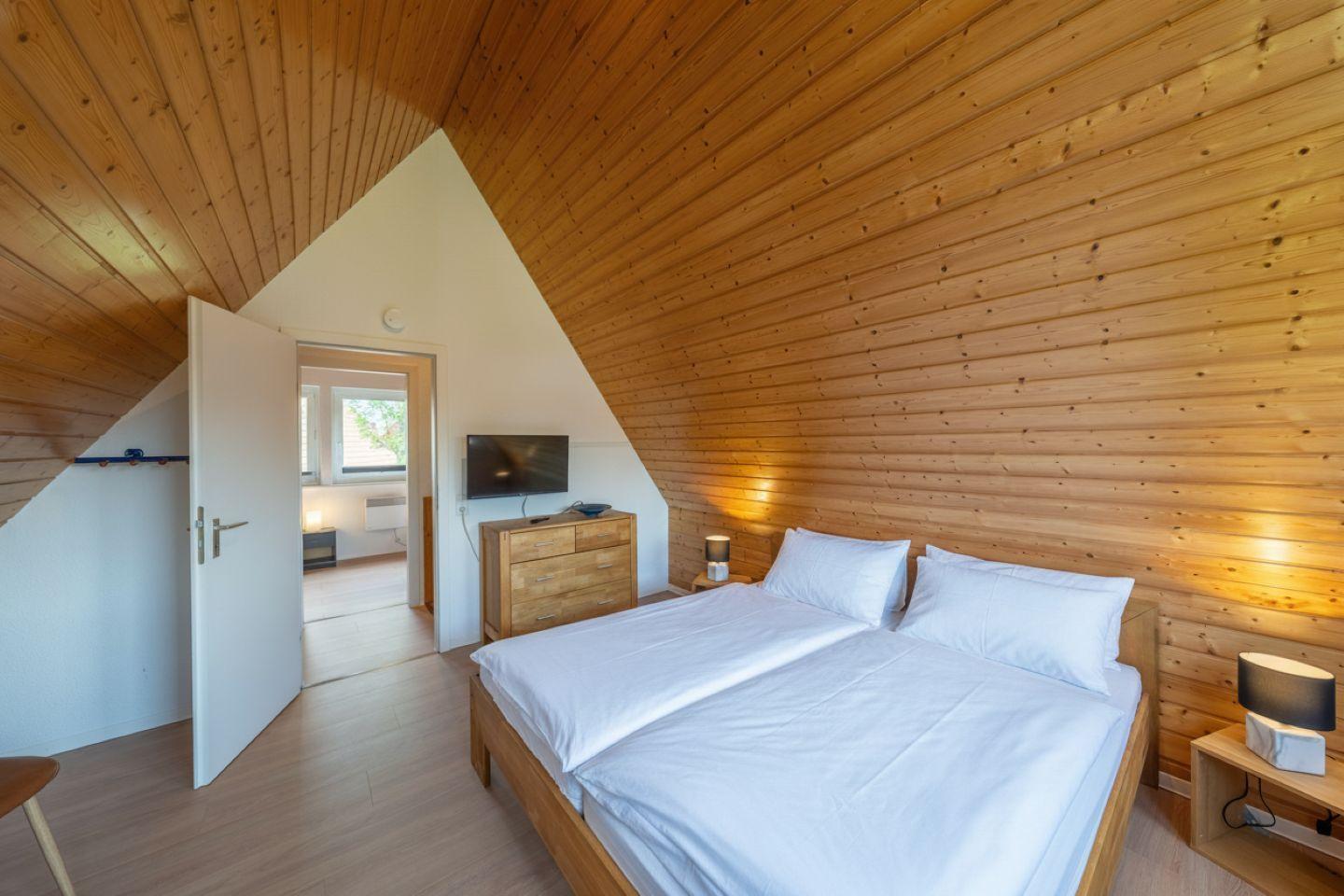 Schlafzimmer mit Holzwand und Doppelbett. TV und Nachttisch sind vorhanden.