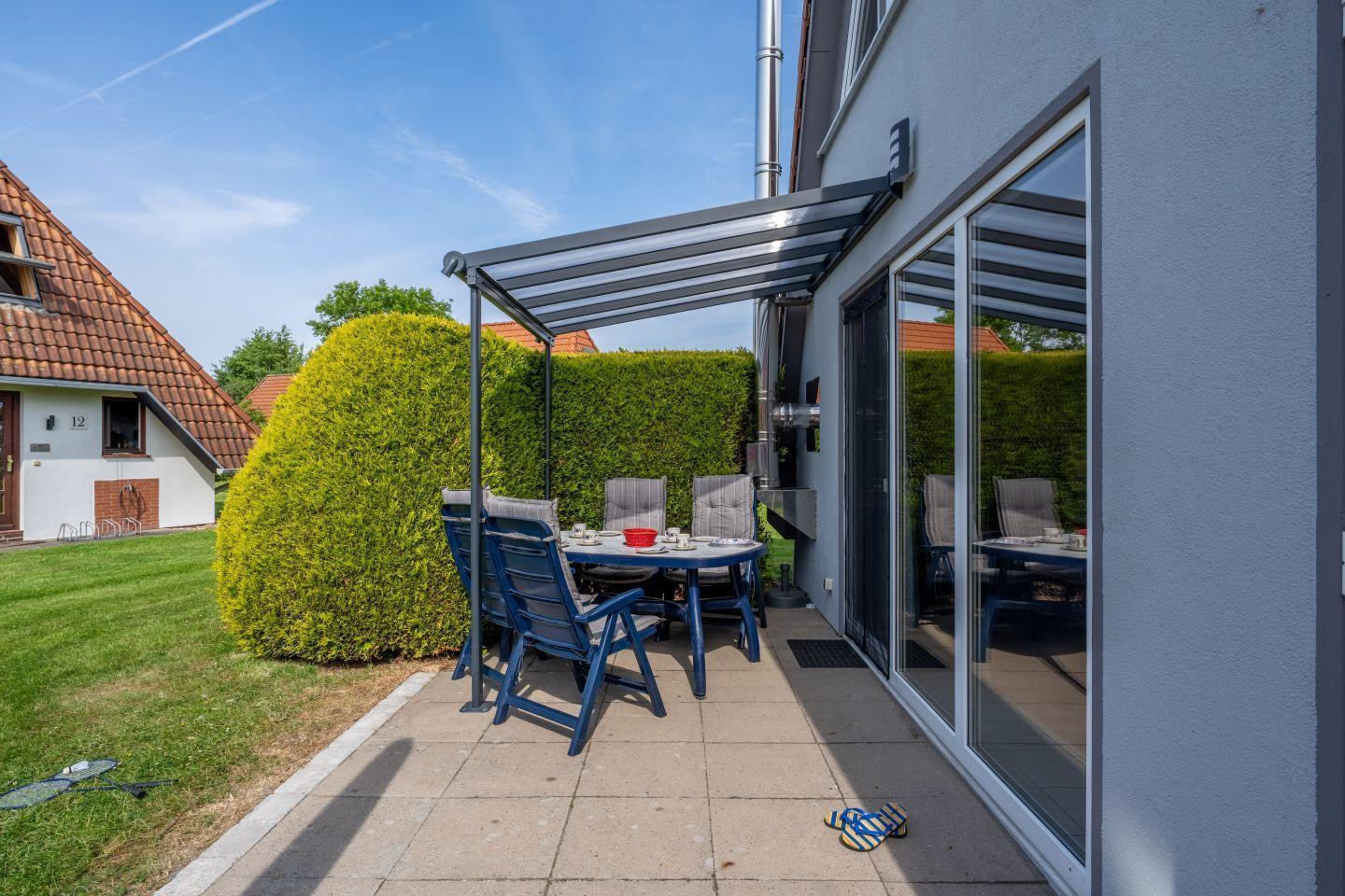 Terrasse mit Sitzgruppe unter Markise. Hinterhof mit Hecke und Rasen.