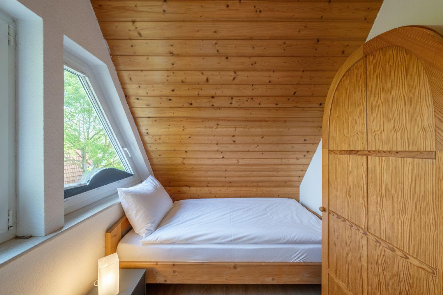 Schlafzimmer mit Dachschrägen, Holzwand, Fenster und Bett.