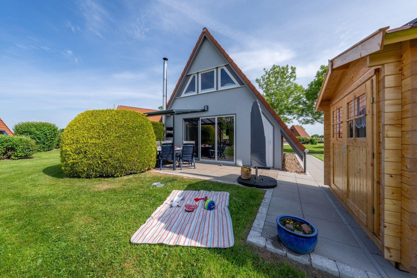 Haus mit Terrasse, Garten und Picknickdecke. Holzschuppen nebenan.
