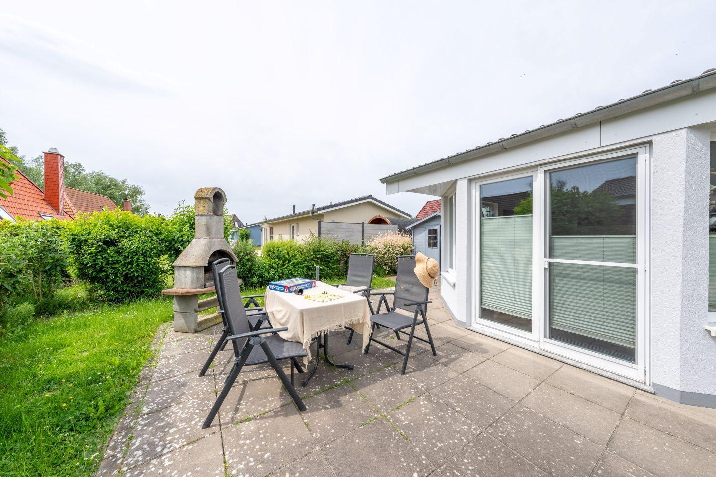 Terrasse mit Tisch, Stühlen und Grillofen. Hinterhof mit Gras und Hecken.