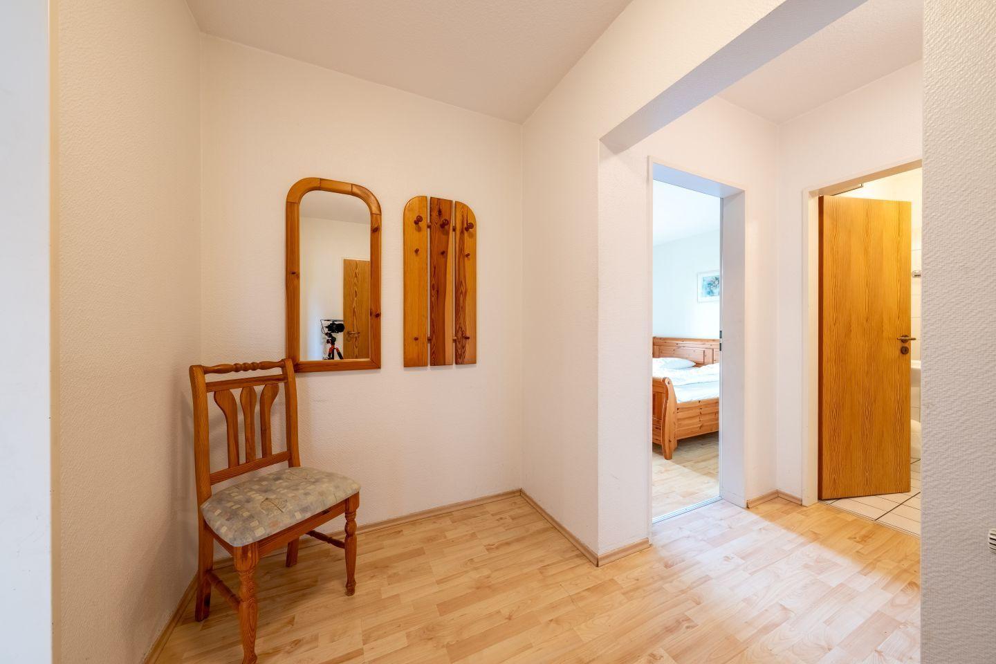 Flur mit Stuhl, Spiegel und Kleiderhaken. Durchgang zu Schlafzimmer und Bad.
