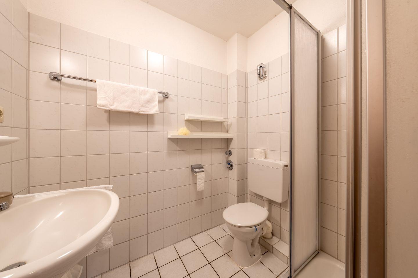 Badezimmer mit Toilette, Dusche, Waschbecken und Handtuchhalter.