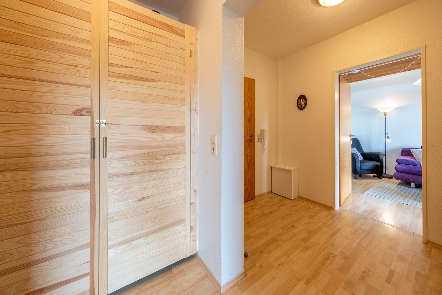 Haus mit Holzschrank, Flur und Blick in Wohnzimmer mit Sofa und Sessel.