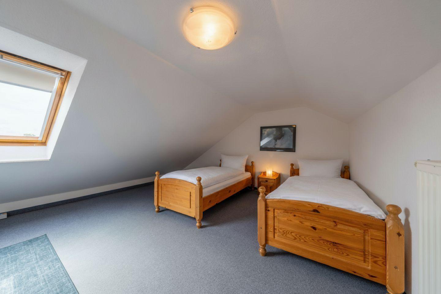 Zwei Einzelbetten, Fenster und Nachttisch in einem Dachzimmer.