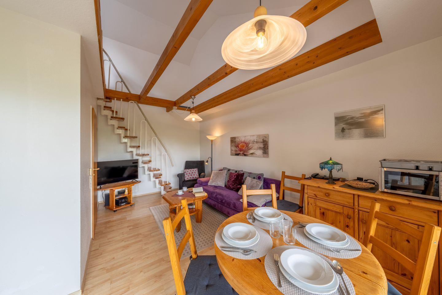 Wohnbereich mit Essplatz, Sofa, TV und Treppe zur oberen Etage.