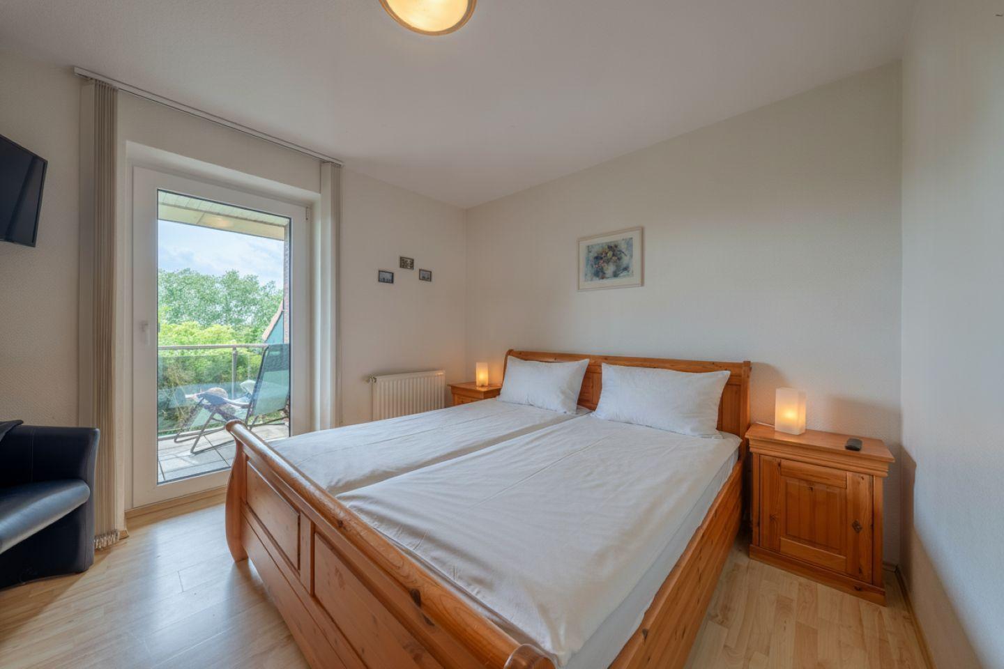 Doppelbett mit Holzrahmen, zwei Nachttische mit Lampe, Balkon mit Gartenblick.