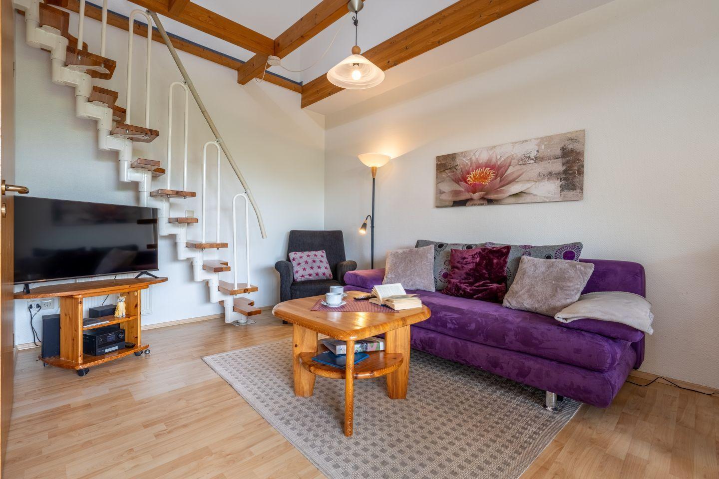 Wohnzimmer mit Sofa, Couchtisch und TV. Treppenhaus führt zur oberen Etage.