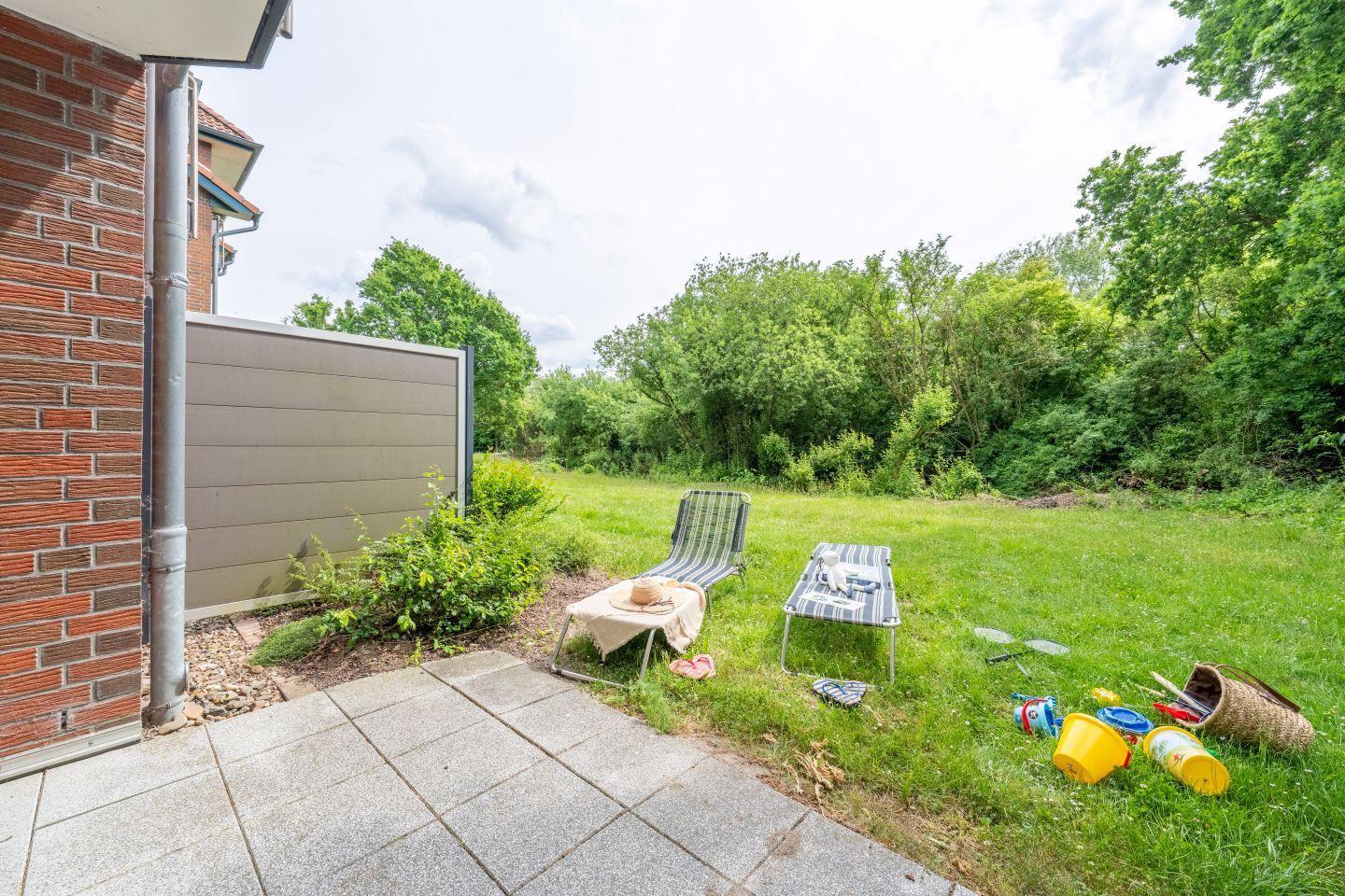 Backyard with lounge chairs and childrens toys on grass area beside house wall.