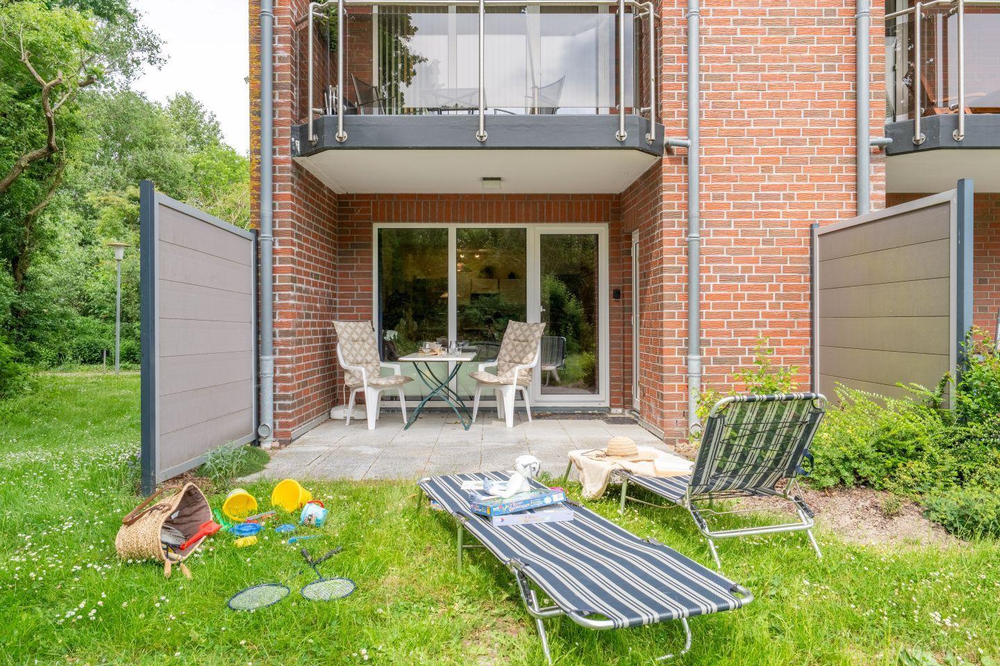 Backyard with lounge chairs, toys, and terrace in front of brick facade.