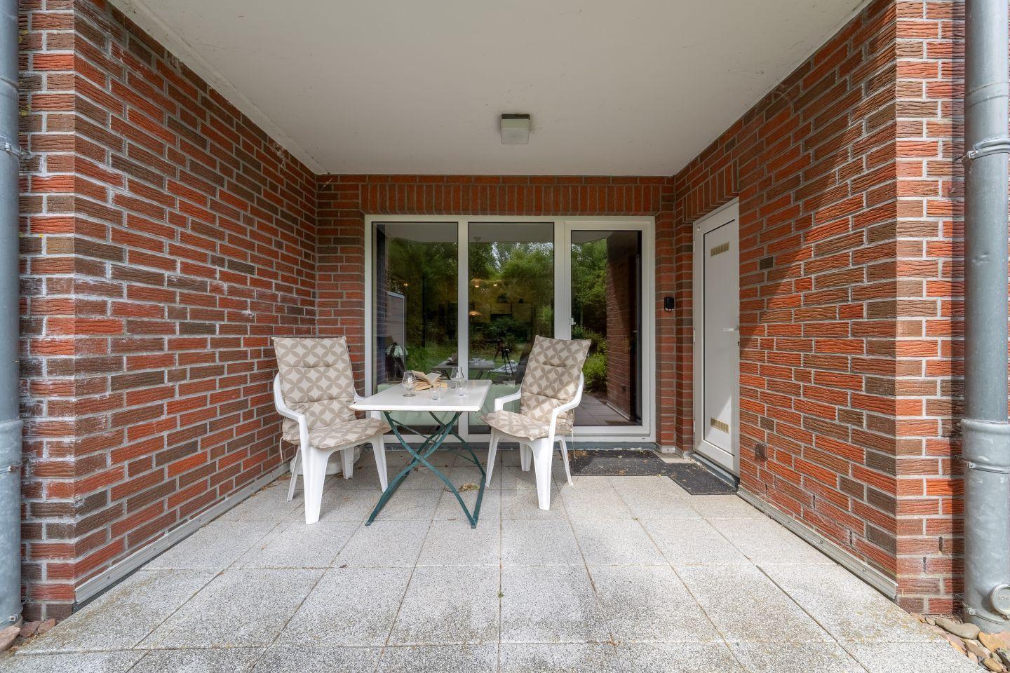 Terrace with table and two chairs, red brick wall, glass door and door.