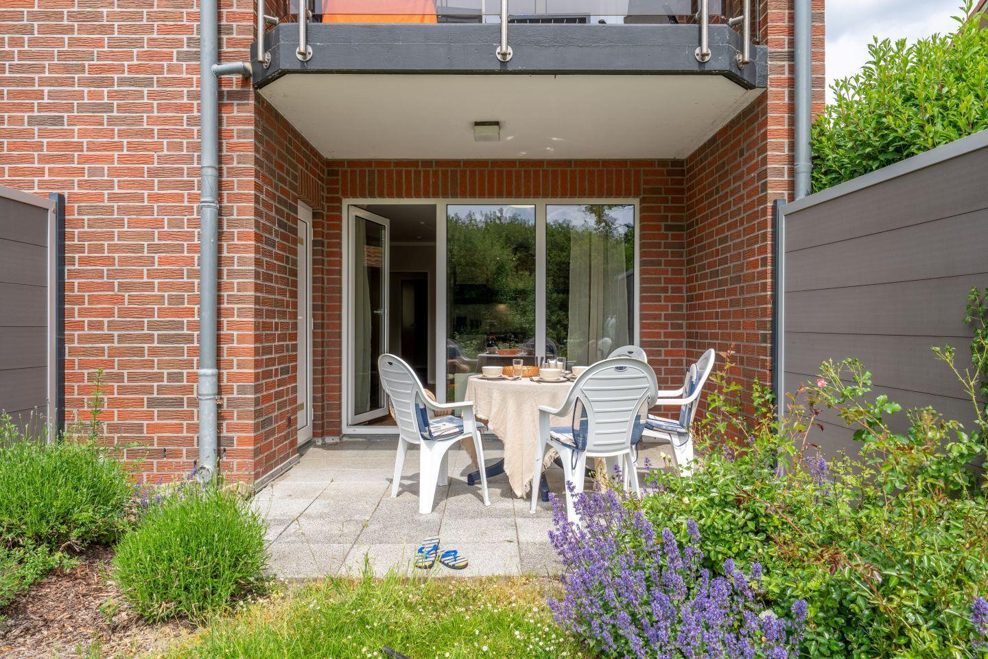 Terrasse mit Tisch und Stühlen, umgeben von Pflanzen und einem Balkon.