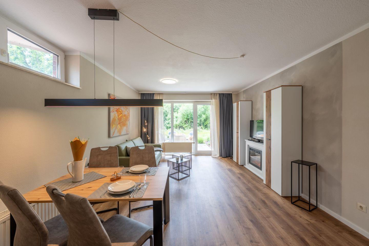 Wohn- und Essbereich mit Holzboden, Esstisch und Sofa. Durchgang zum Garten.