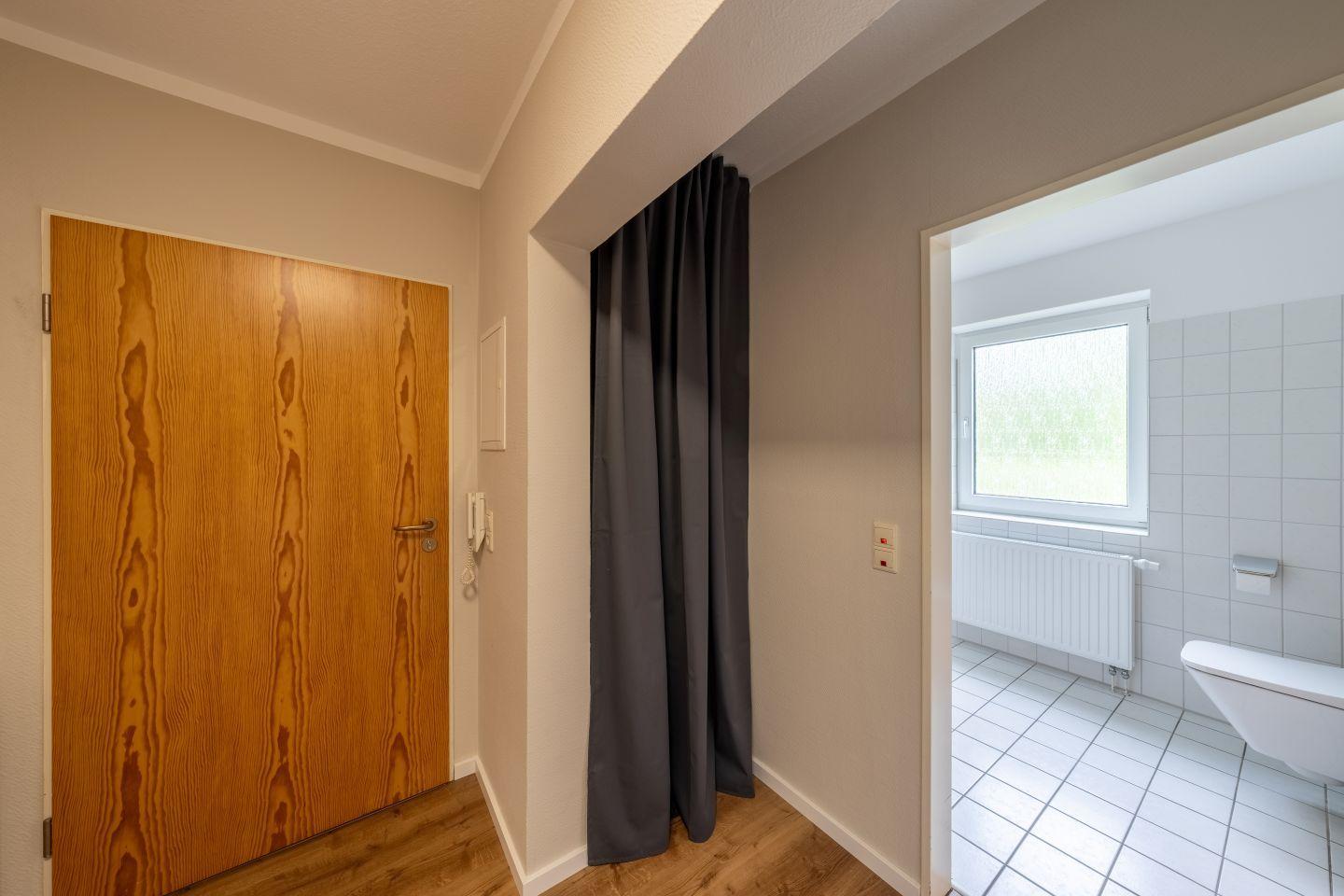 Flur mit Holztür und Vorhang, Blick in Bad mit Toilette und Fenster.