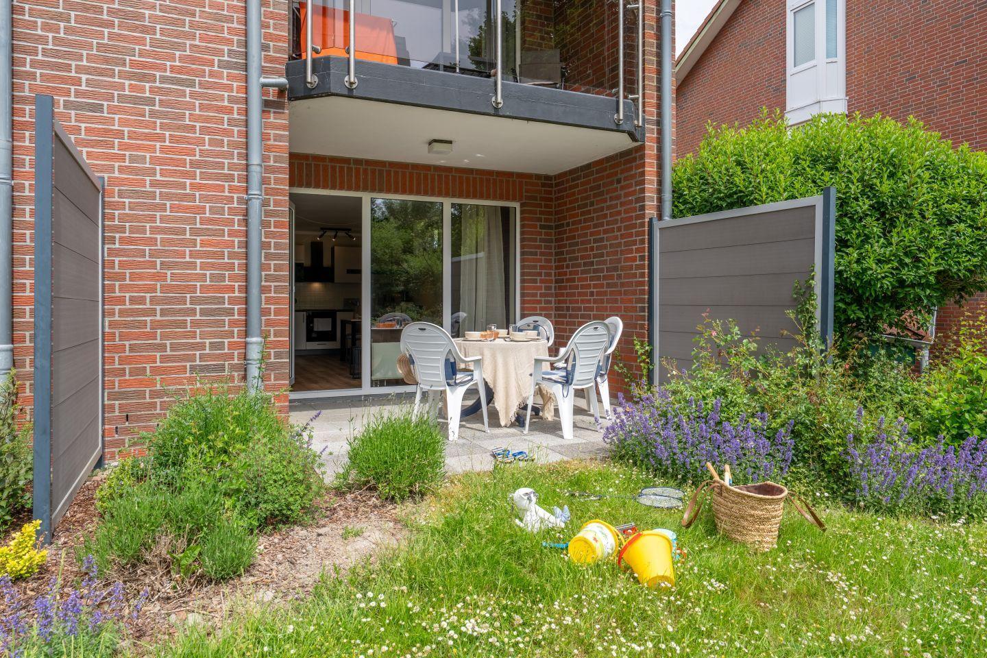 Terrasse mit Tisch und Stühlen, Blick in die Küche, Garten mit Blumen und Spielzeug.