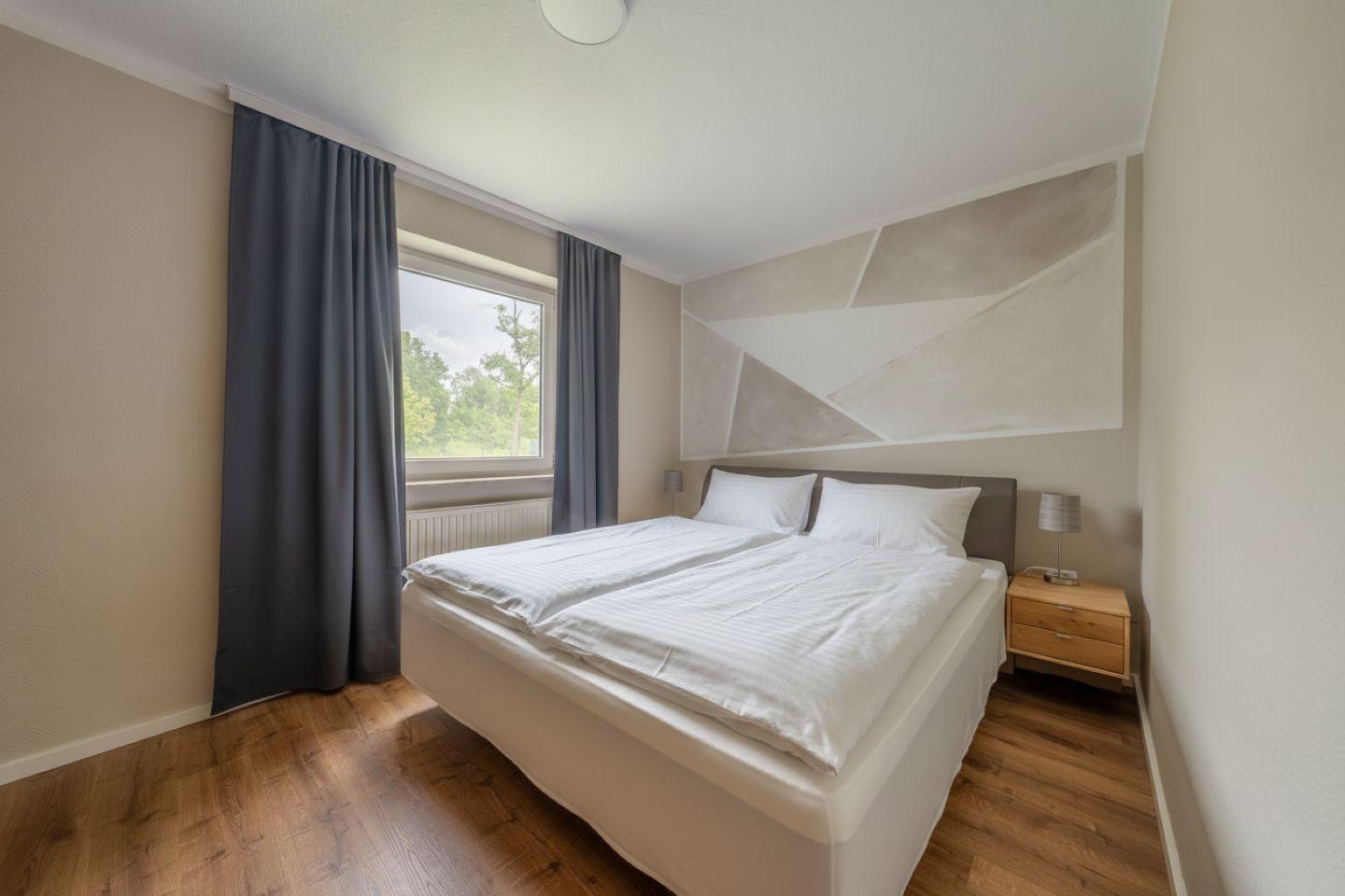 Schlafzimmer mit Doppelbett, Fenster und Holzboden.