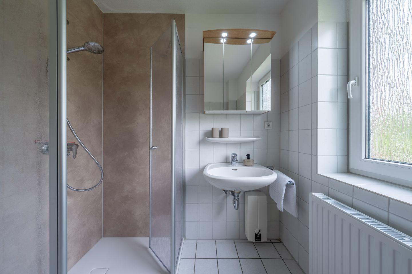 Badezimmer mit Dusche, Waschbecken und Spiegel