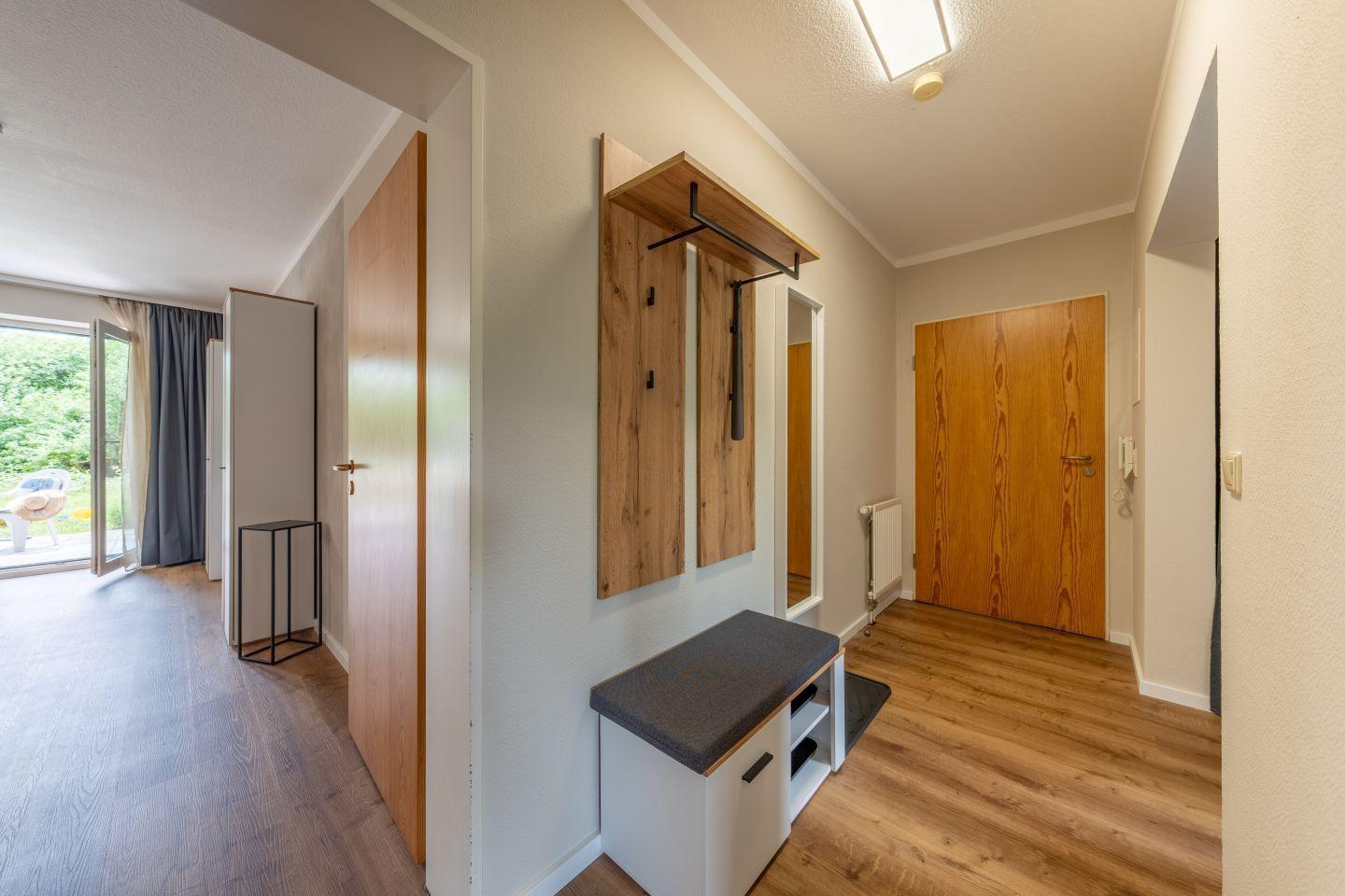 Flur mit Holztür, Garderobe und Sitzbank. Durchgang zu Wohnbereich mit Terrasse.