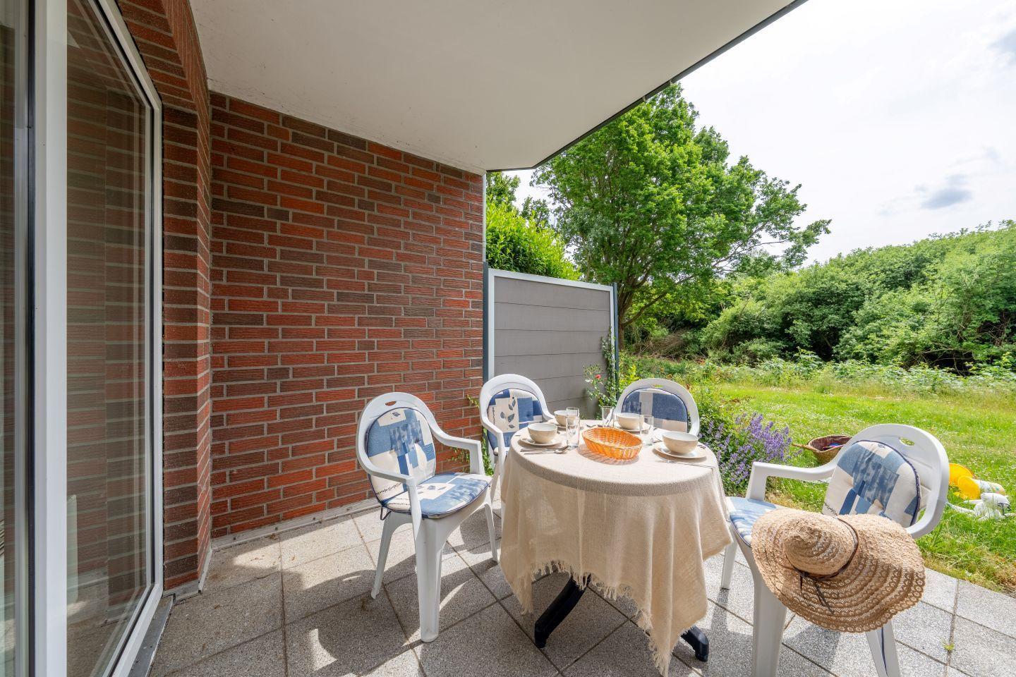 Terrasse mit Tisch und Stühlen, Blick auf grüne Wiesen und Bäume.