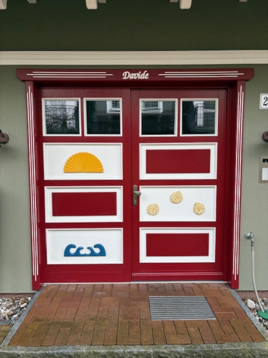 Rote Haustür mit weißen Paneelen und Meeresmotiven wie Muscheln und Wellen.