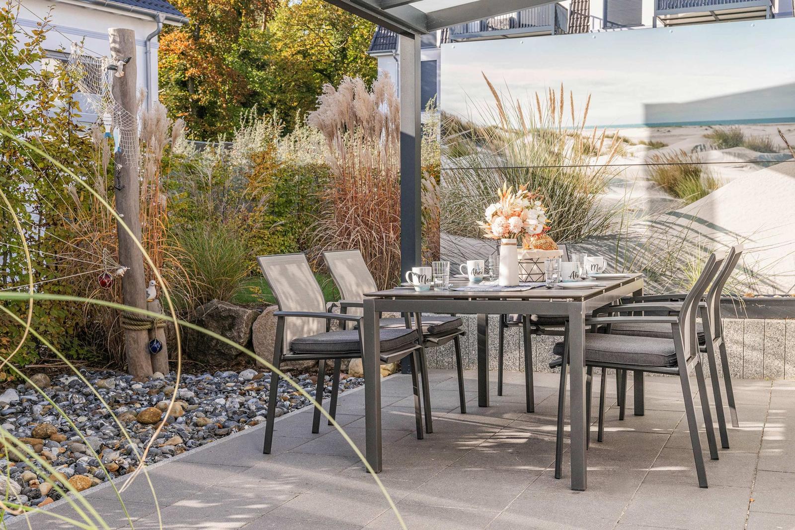Terrasse mit Tisch und Stühlen, Pflanzen und Blick auf Dünen.