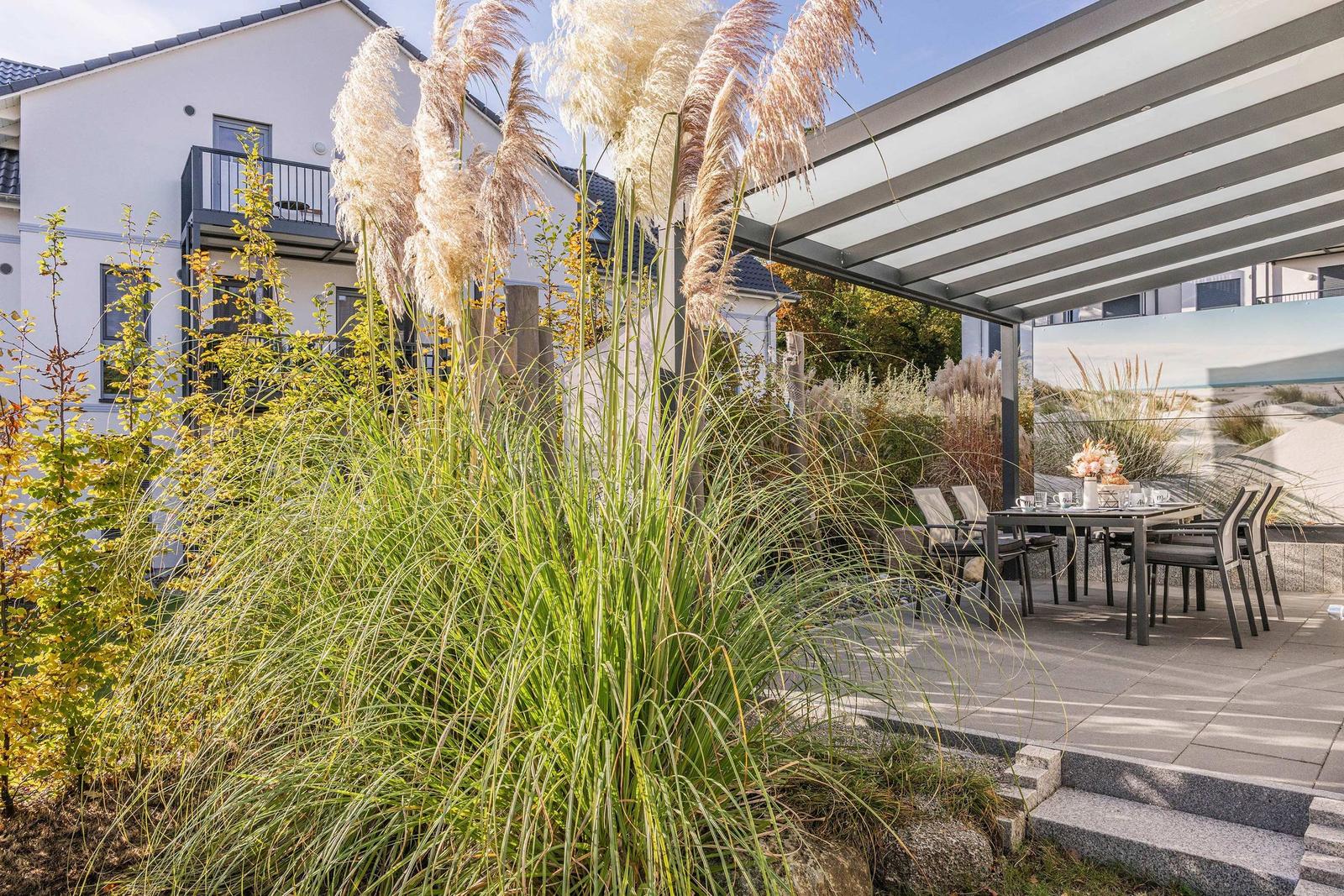 Terrasse mit Sitzgruppe unter Markise, umgeben von Gräsern und Pampasgras.