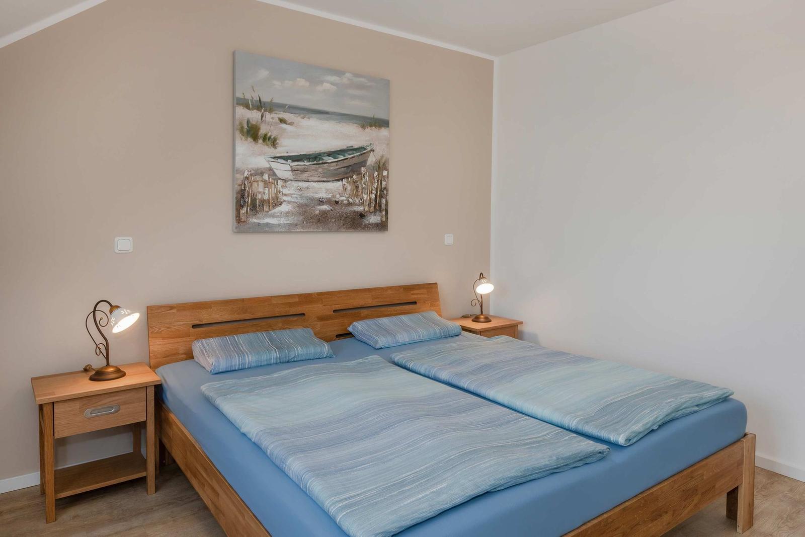 Doppelbett mit Holzrahmen, zwei Nachttische mit Lampen und Wandbild mit Boot.