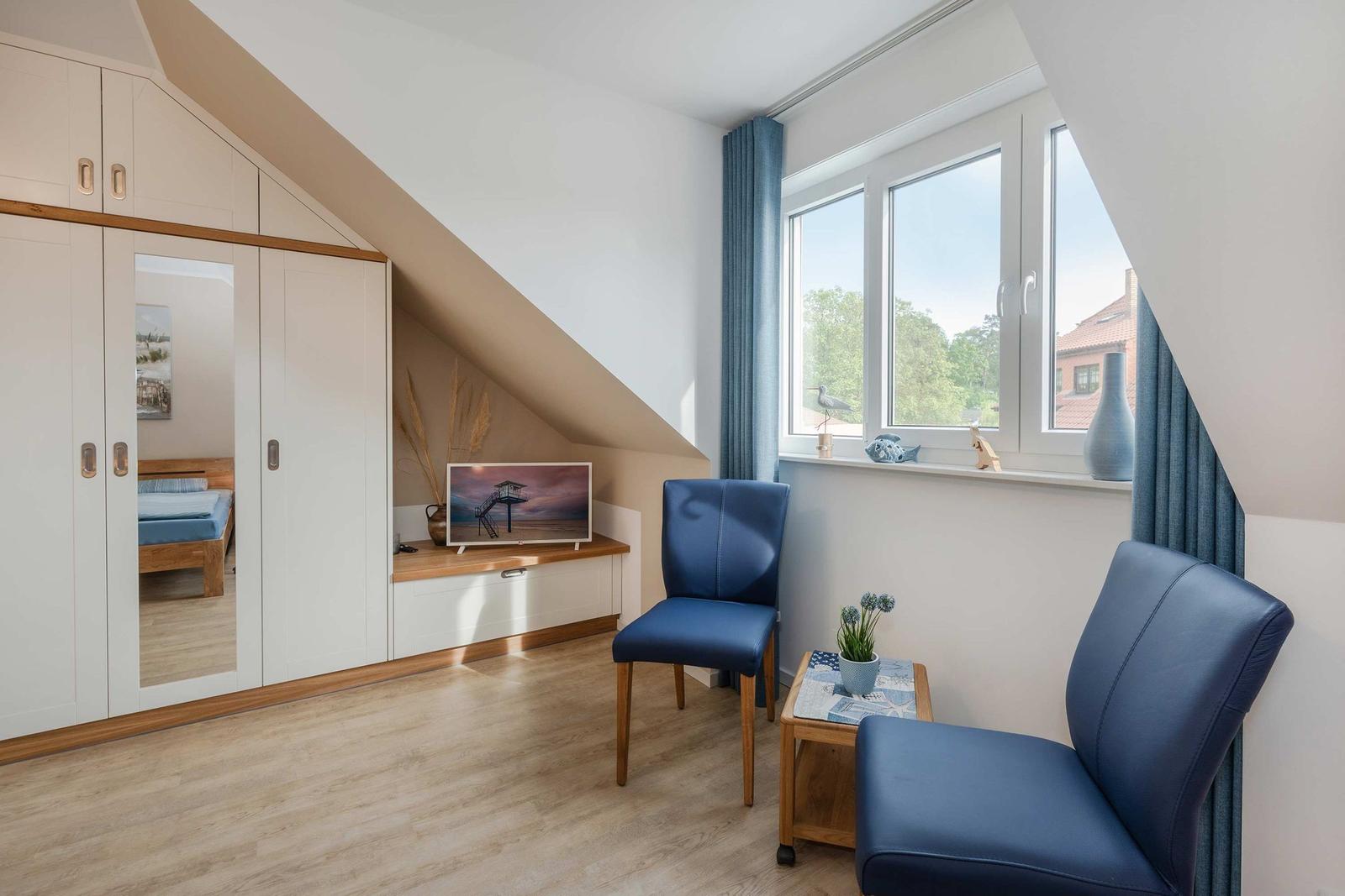 Zimmer mit Dachschrägen, blauen Stühlen, Fenster und Kleiderschrank.