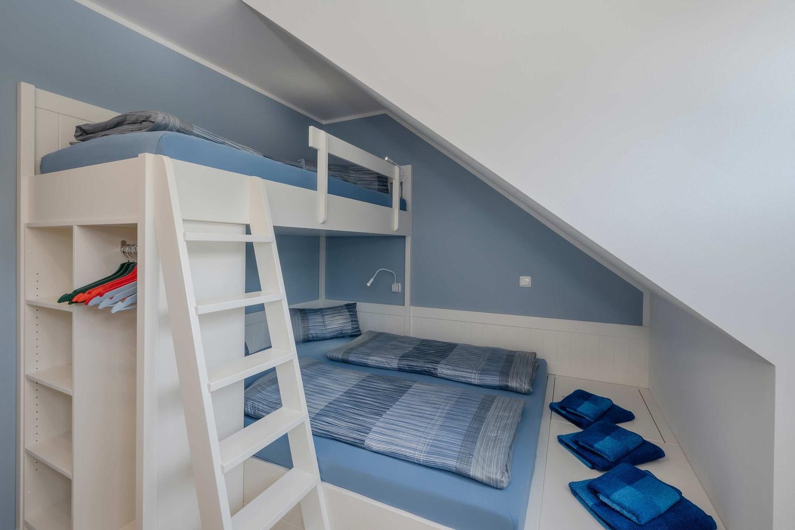 Zimmer mit Doppelstockbett, Kleiderständer und gefalteten Handtüchern.