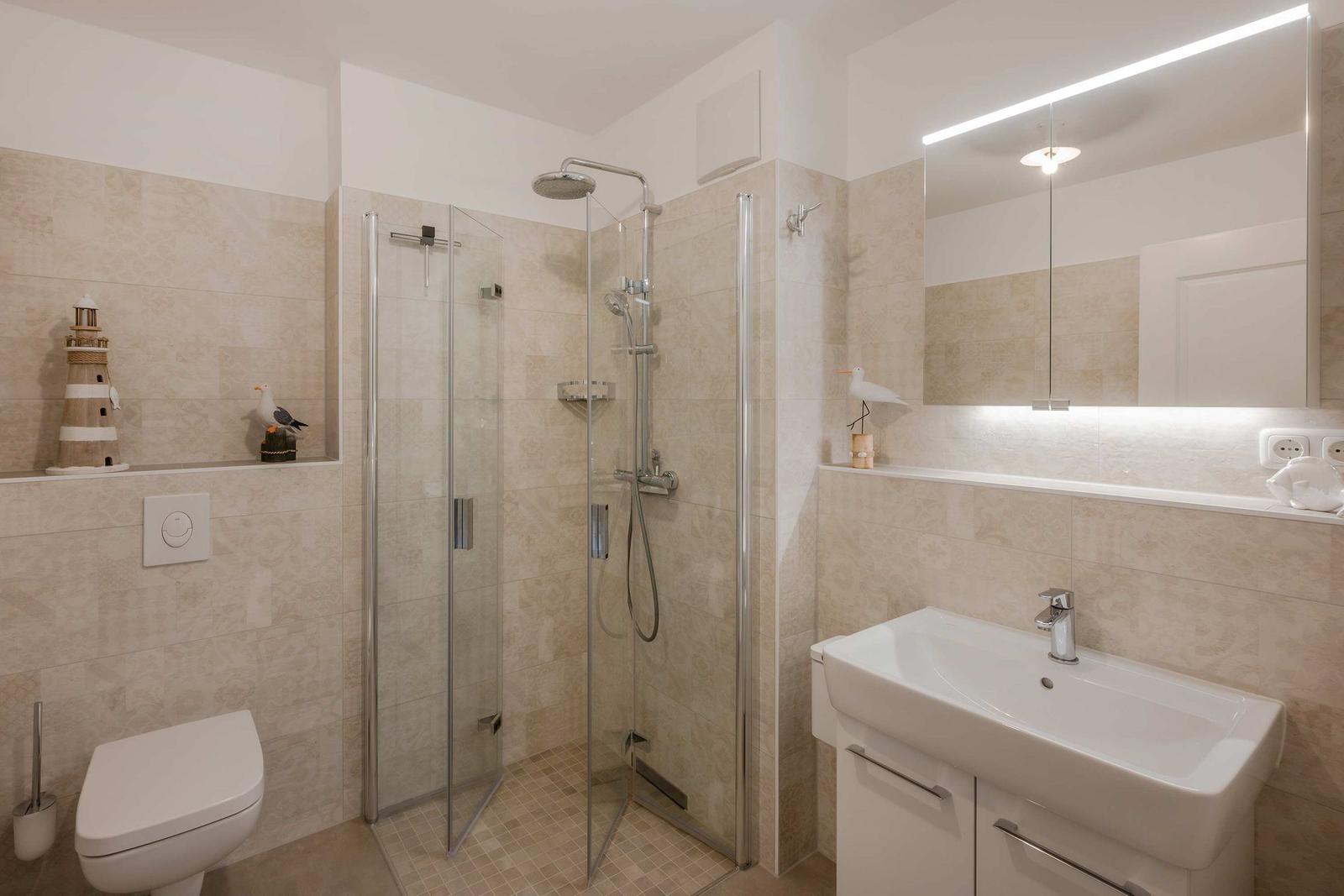 Badezimmer mit Dusche, Waschbecken und Toilette. Wandgestaltung mit hellen Fliesen.