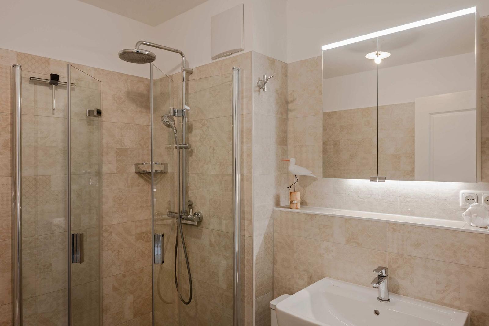 Dusche mit Glaswand, Waschbecken und beleuchtetem Spiegel